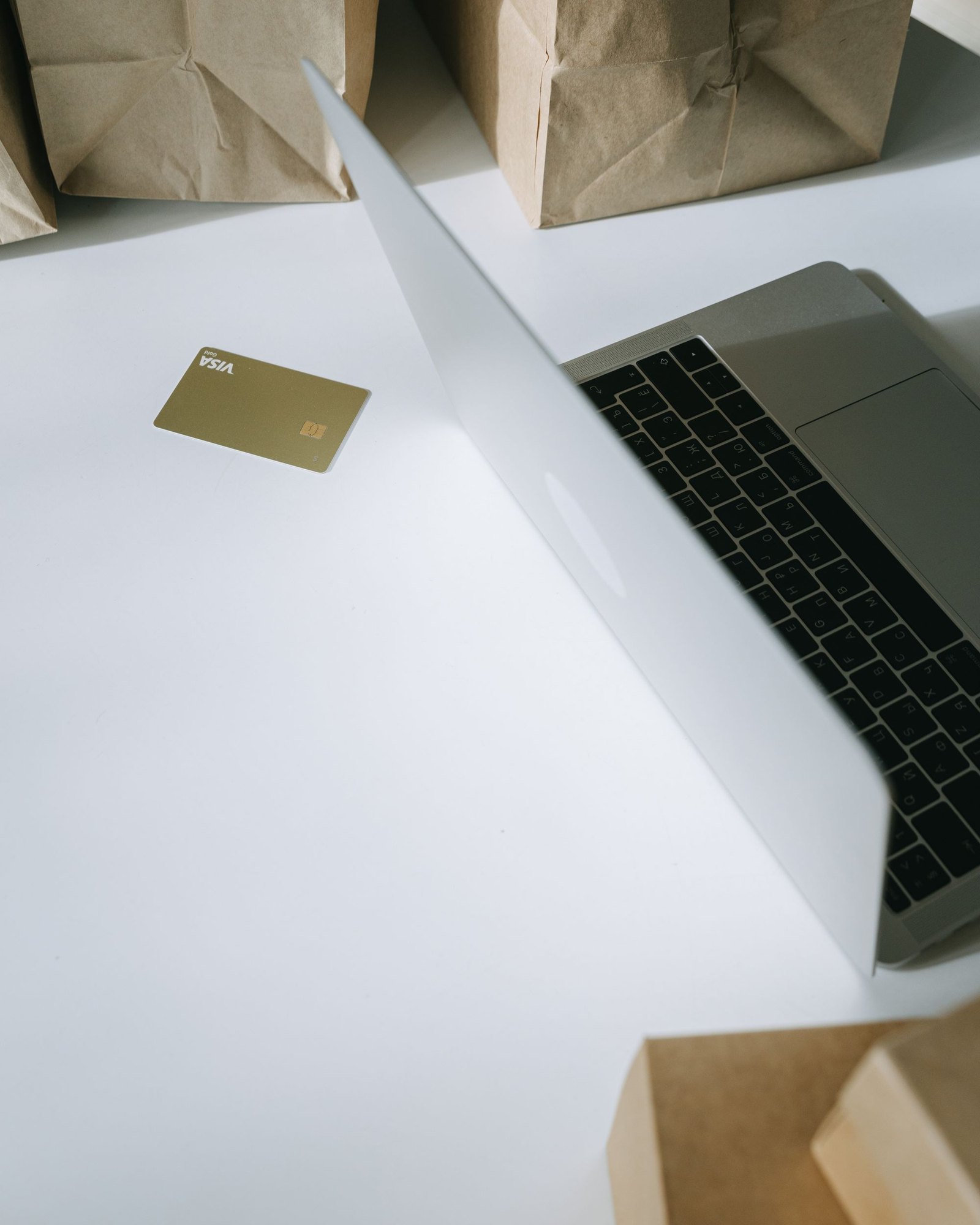 Laptop, payment card and paper shopping bags on a white desk